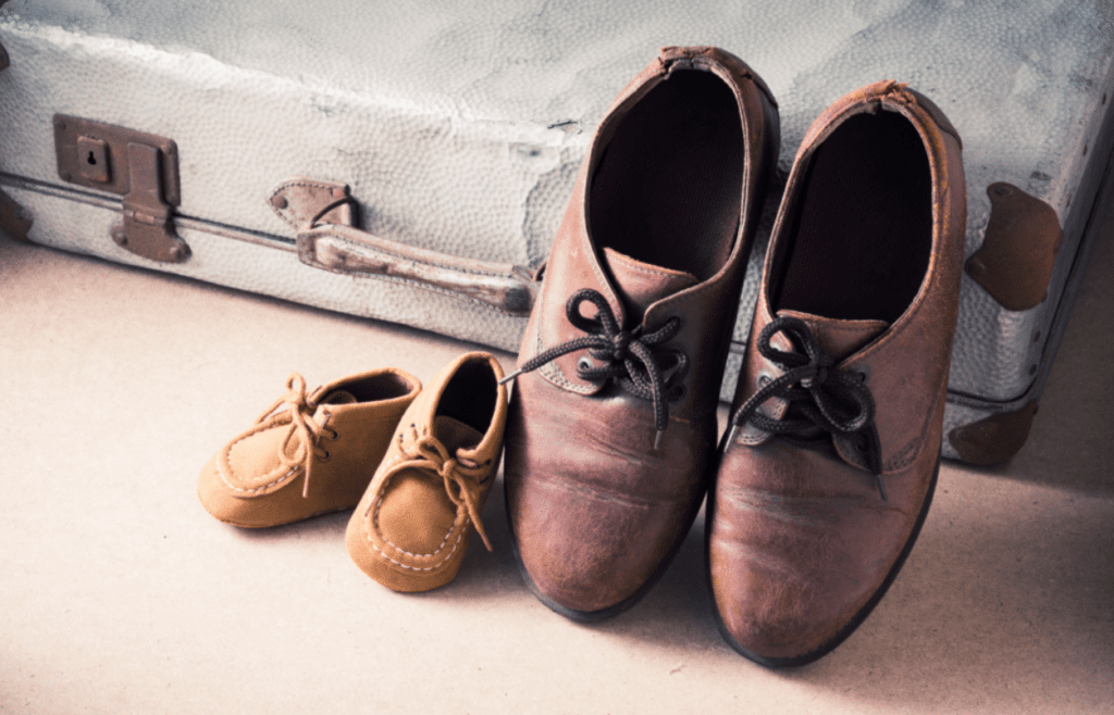 Adults shoes and kids shoes leaning against a suitcase.