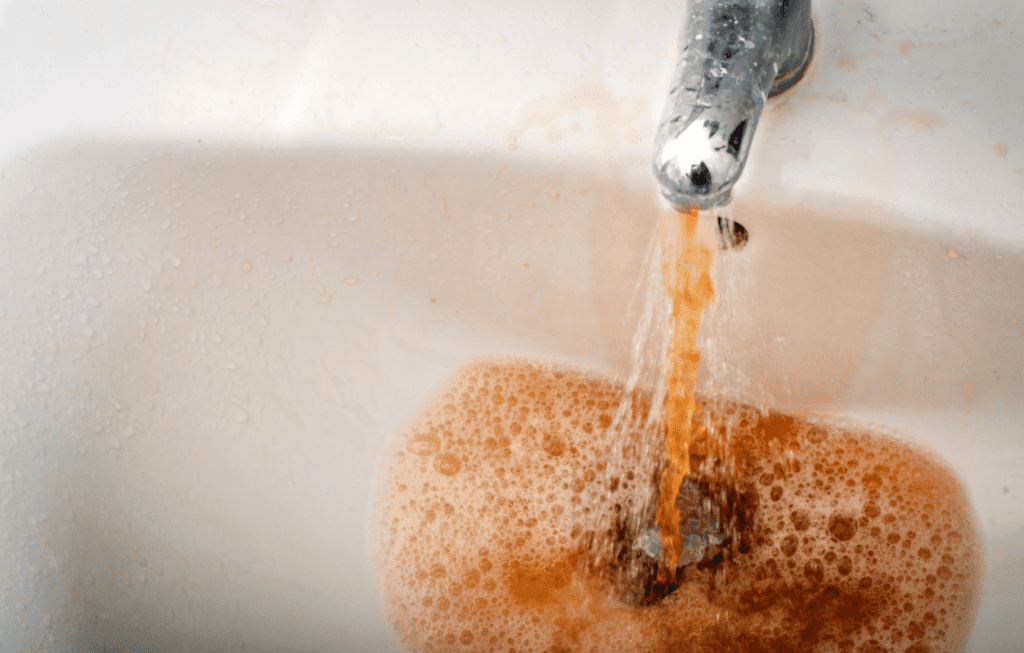 Brown dirty water coming out of a silver faucet into a white sink.