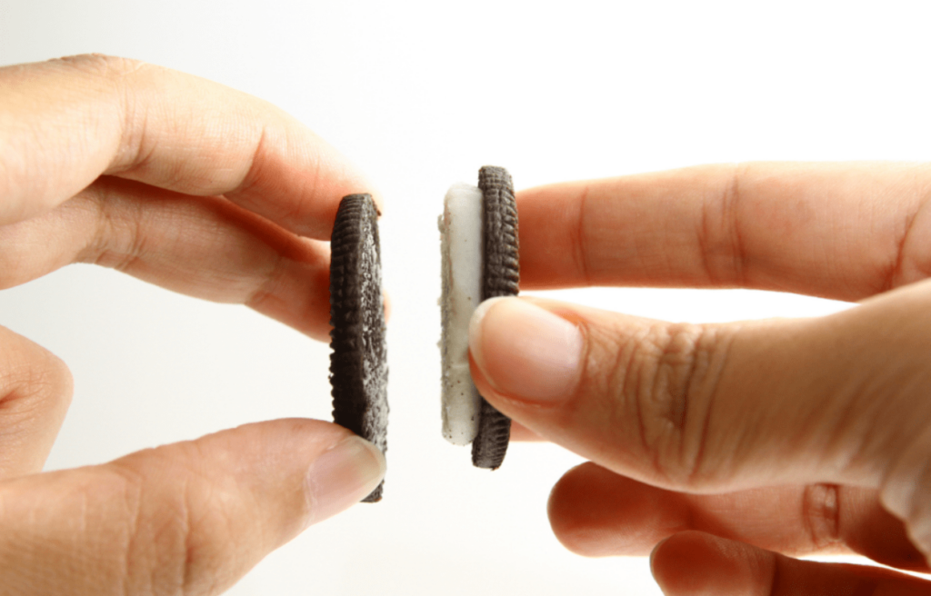 Somebody pulls apart a black oreo cookie with white frosting.