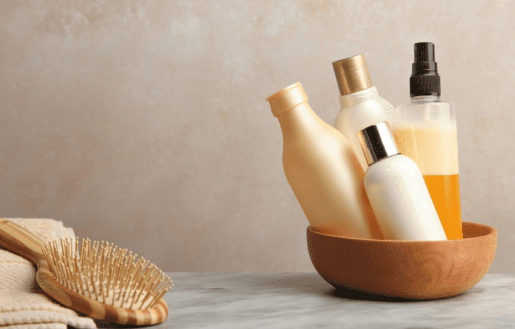 Shampoo and conditioner and other hair products in a bowl with a hair brush and towel.