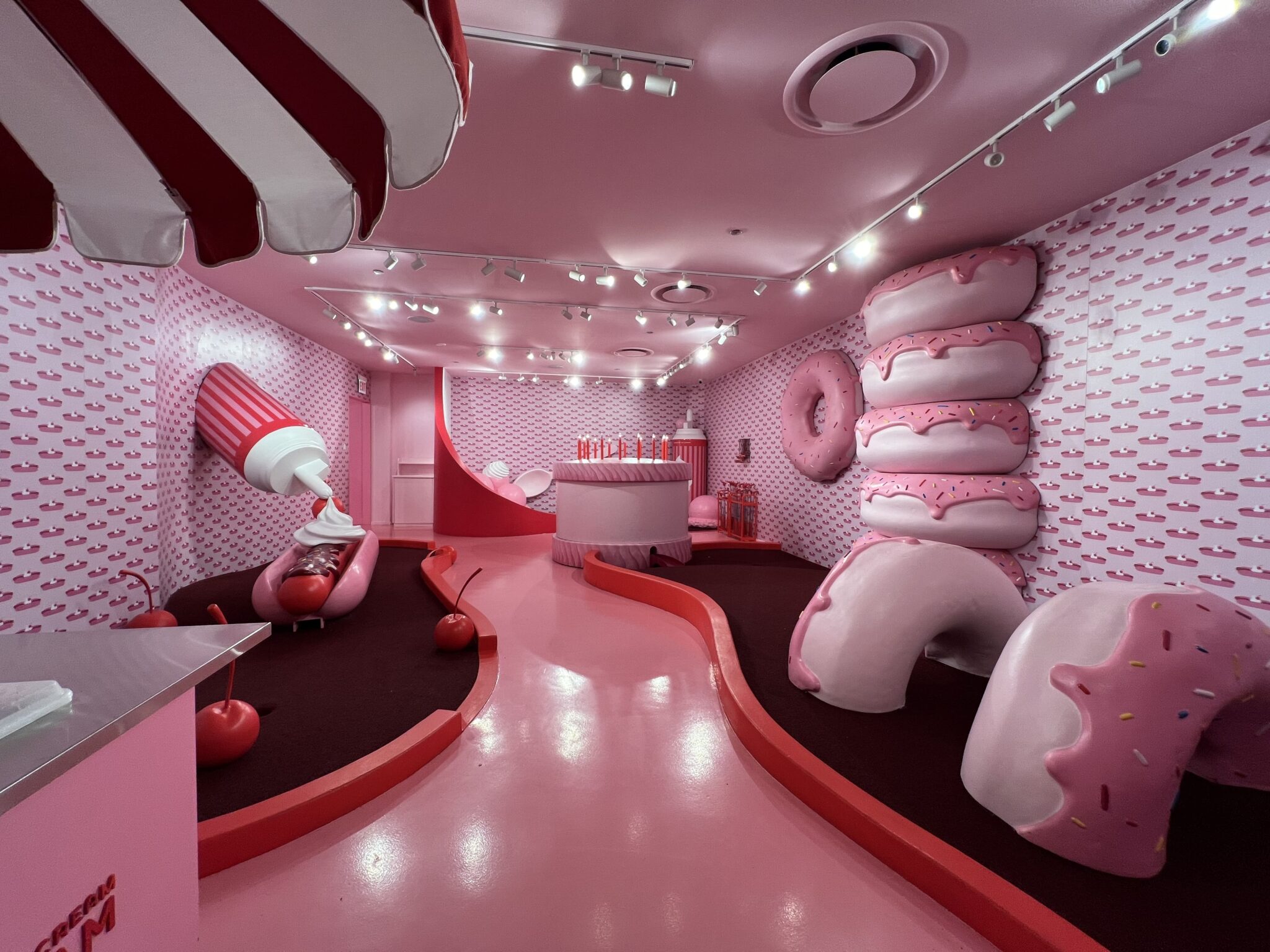 Whimsical pink room at the Museum of Ice Cream in Chicago, featuring oversized donut sculptures, cherries, and a giant ice cream cone