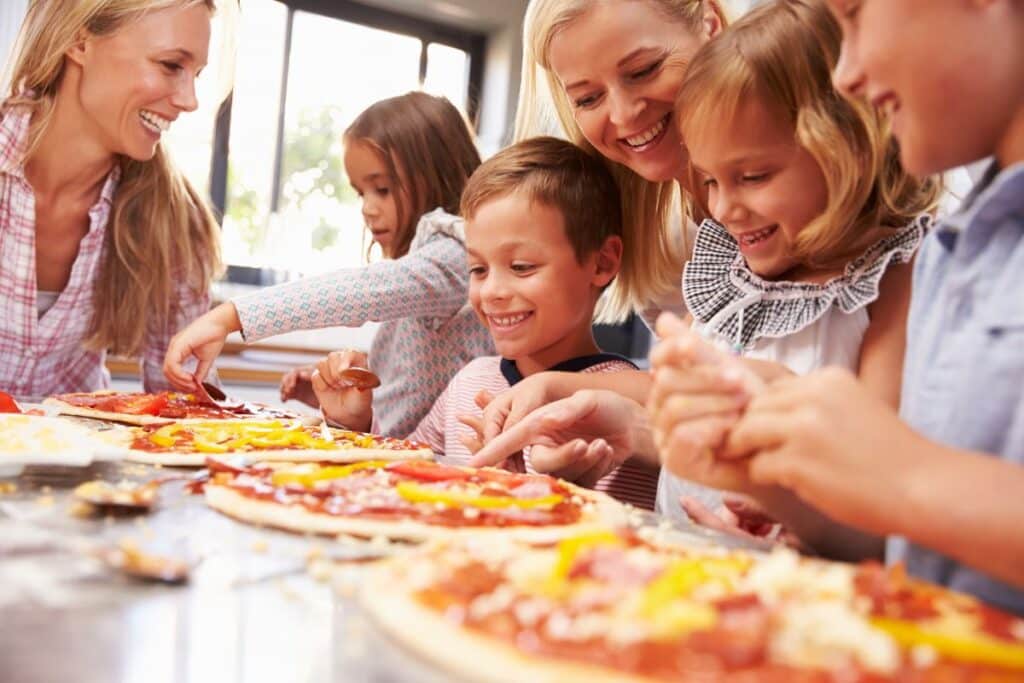 Two mothers assisting kids on how make pizzas in a pizza party for three year olds.