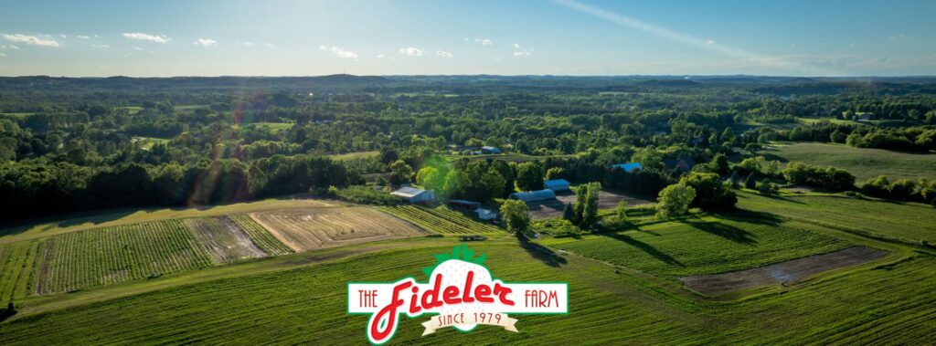 Aerial view of Fideler Farm in Kewaskum, Wisconsin, showing wide-open green fields and surrounding forest