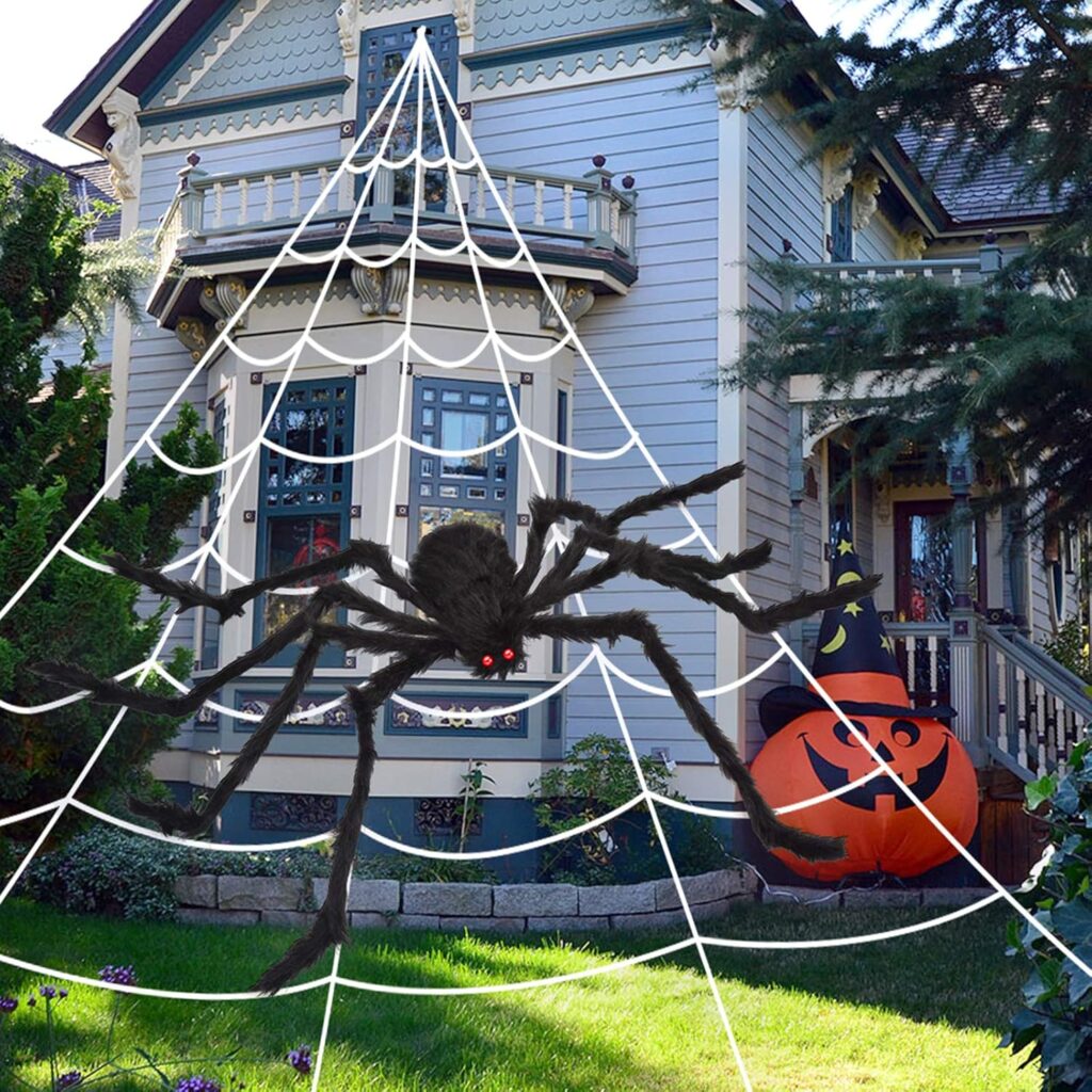 Giant fake spider with fake spider web attached to the home and a giant jack o'lantern beside the porch