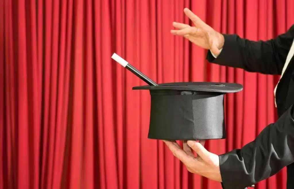 Magician performing a trick with a top hat on stage in front of red curtain