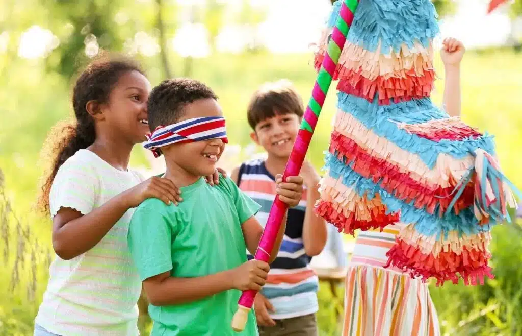 Kids taking turns hitting a colorful piñata outdoors with one kid being blindfolded