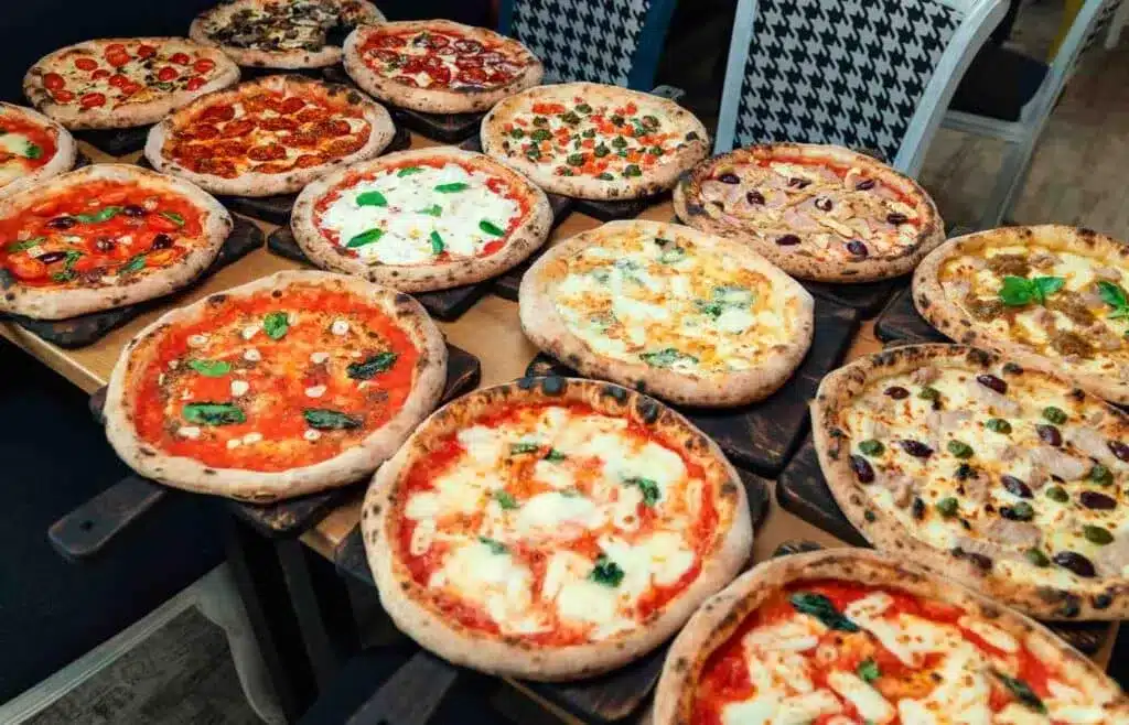 Different kidns of freshly baked pizzas with basil, cheese, olives, tomatoes as toppings