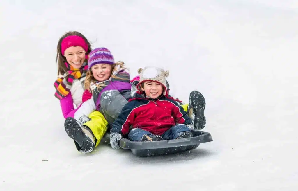 Children sledding down a snowy hill with an adult