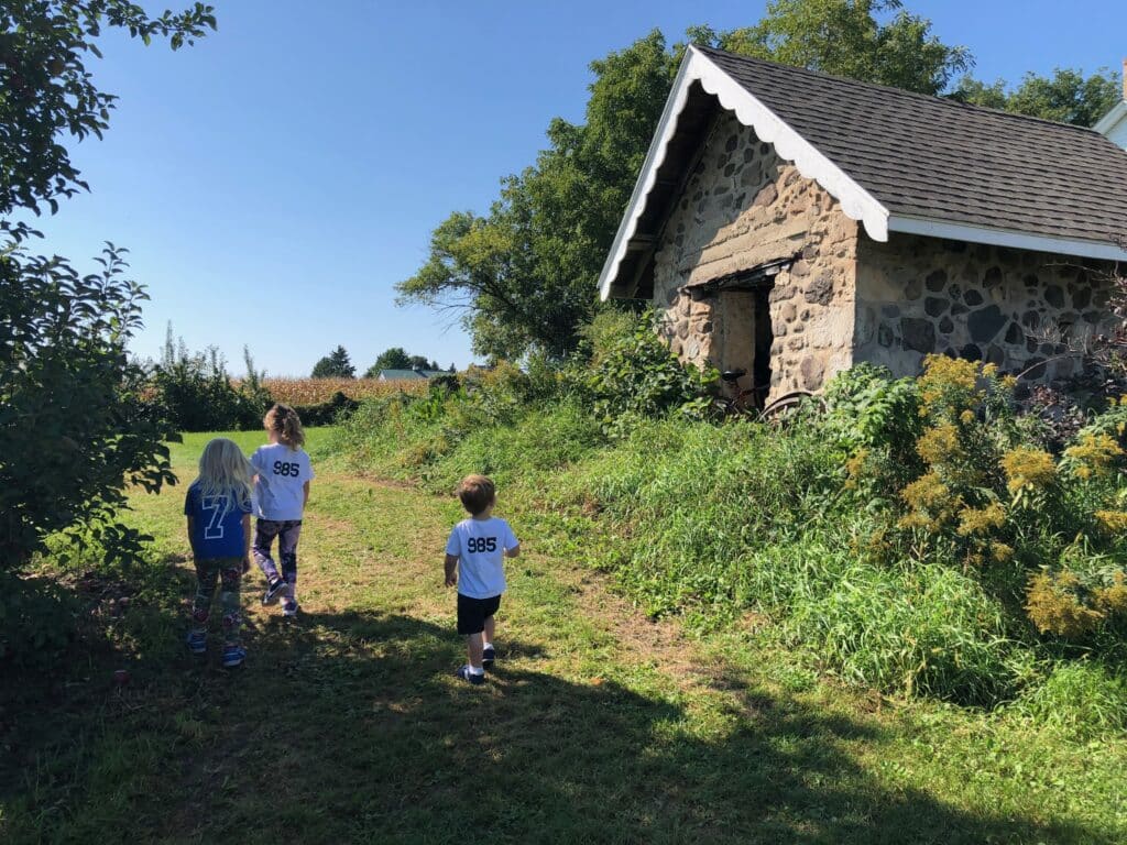 Three young children walking through grassy paths near a stone outbuilding at Barthel Fruit Farm in Mequon.