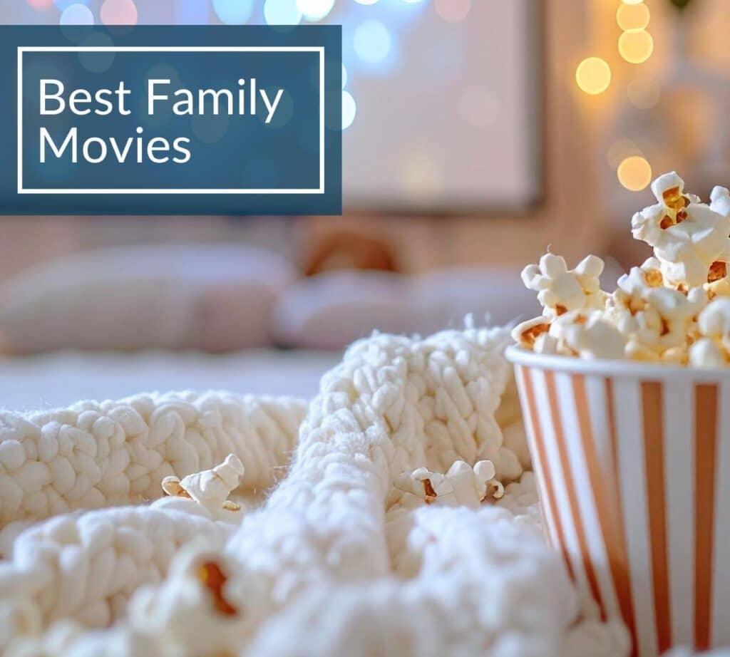 Cozy family movie night setup with popcorn in a striped cup, warm blanket, and blurred lights in the background. Text overlay reads ‘Best Family Movies