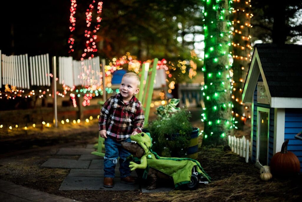 Little boy in plaid shirt with his dachsund in lizard costume at Happily Haunted Gardens at Bookworm Gardens in Sheboygan.