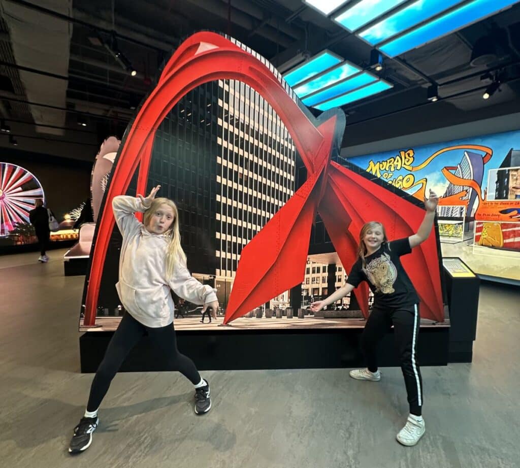 Children pose playfully in front of colorful Chicago murals and sculptures inside the Skydeck’s interactive exhibit area.