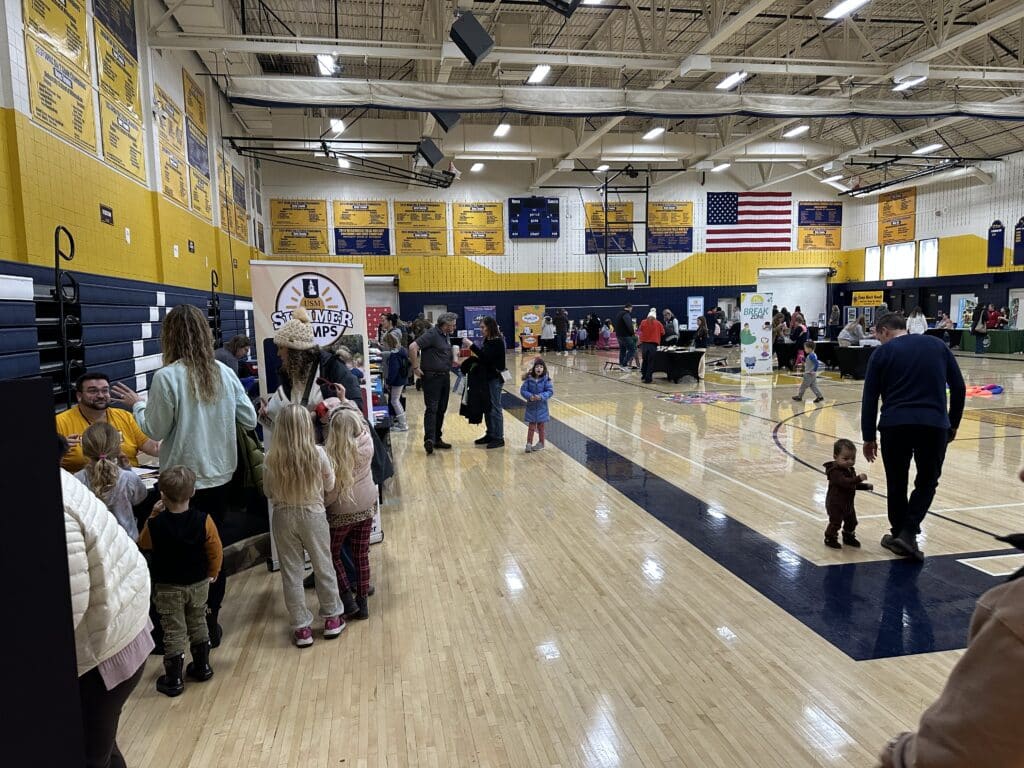 Families explore booths at the Milwaukee Camp Fair at University School of Milwaukee, with camps and activities set up around the gym