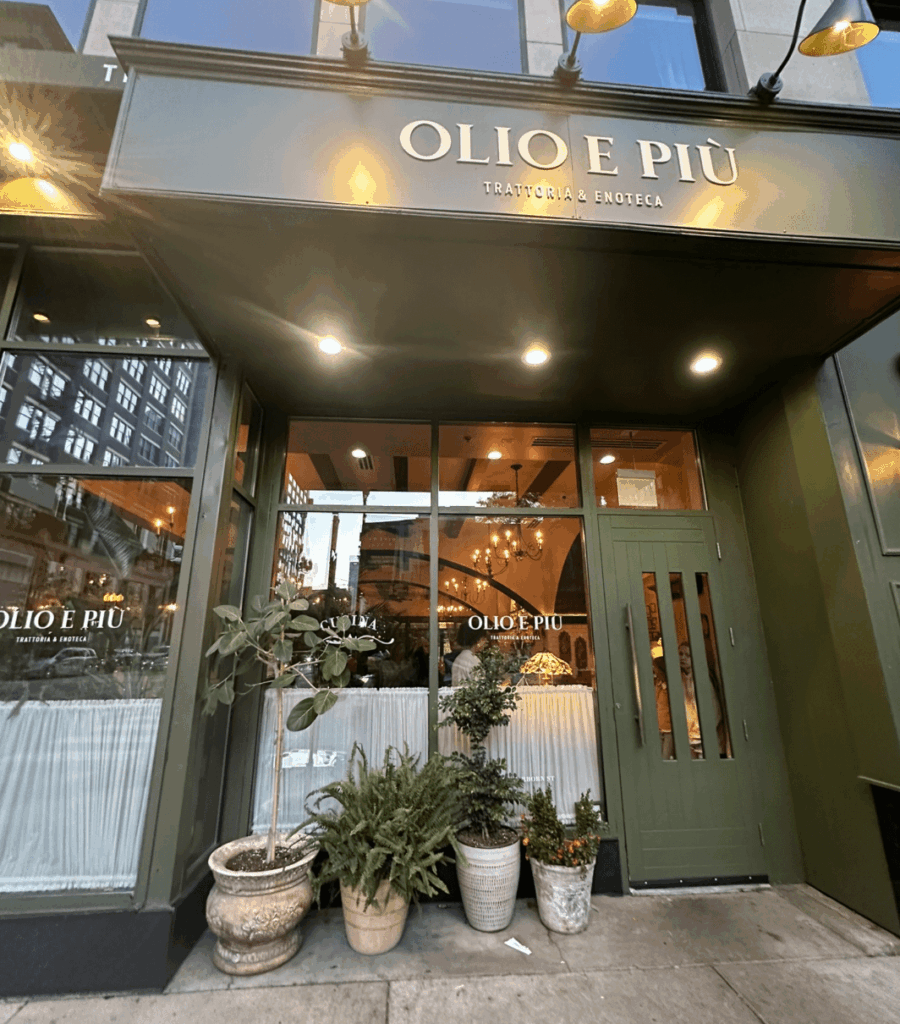 Exterior of Olio e Più restaurant in downtown Chicago, an Italian trattoria with green facade, large windows, and potted plants at the entrance.