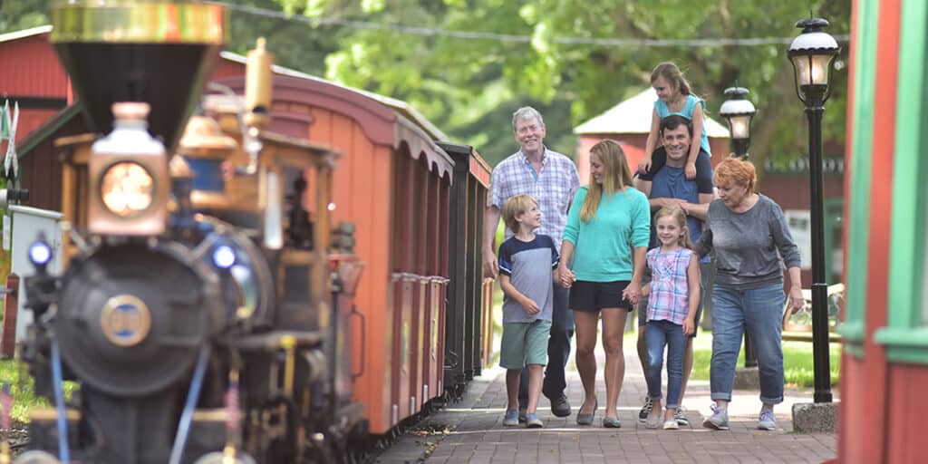 Multi-generational family walking next to a miniature steam train at Riverside & Great Northern Railway in Wisconsin Dells.
