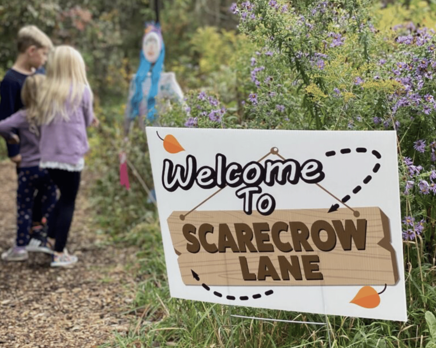 Two children start down the path of Scarecrow Lane, walking past a large sign that says "Scarecrow Lane" at Retzer Nature Center