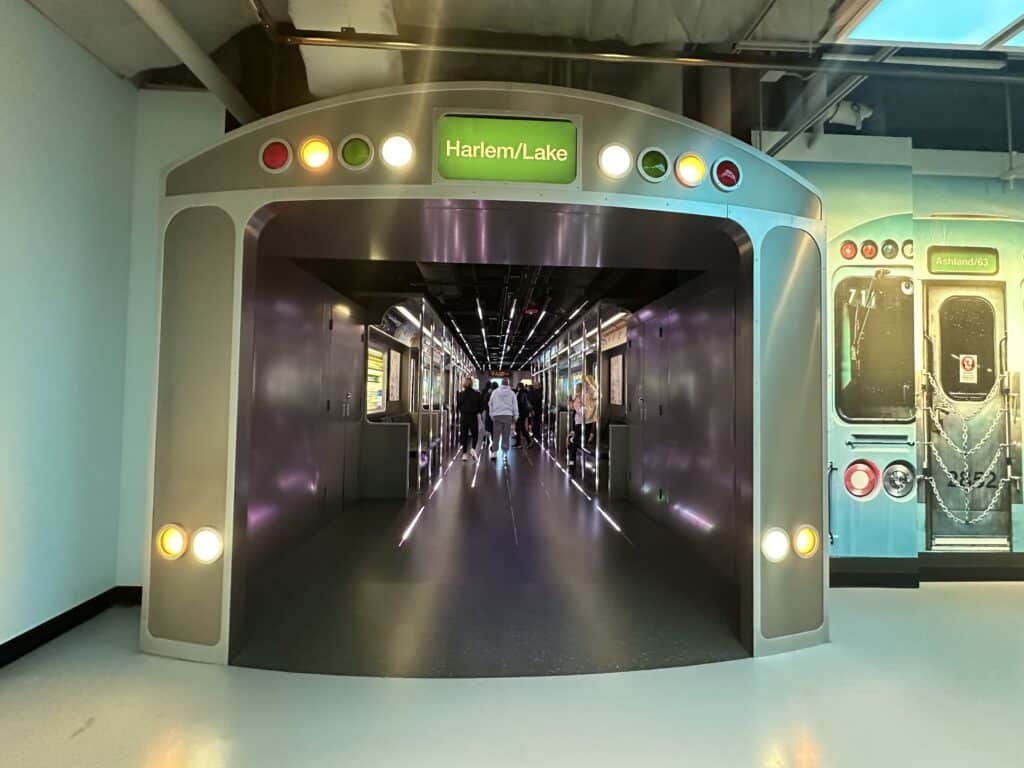Families walk through a train-themed tunnel exhibit inside Skydeck Chicago, designed to look like a Chicago “L” train car.