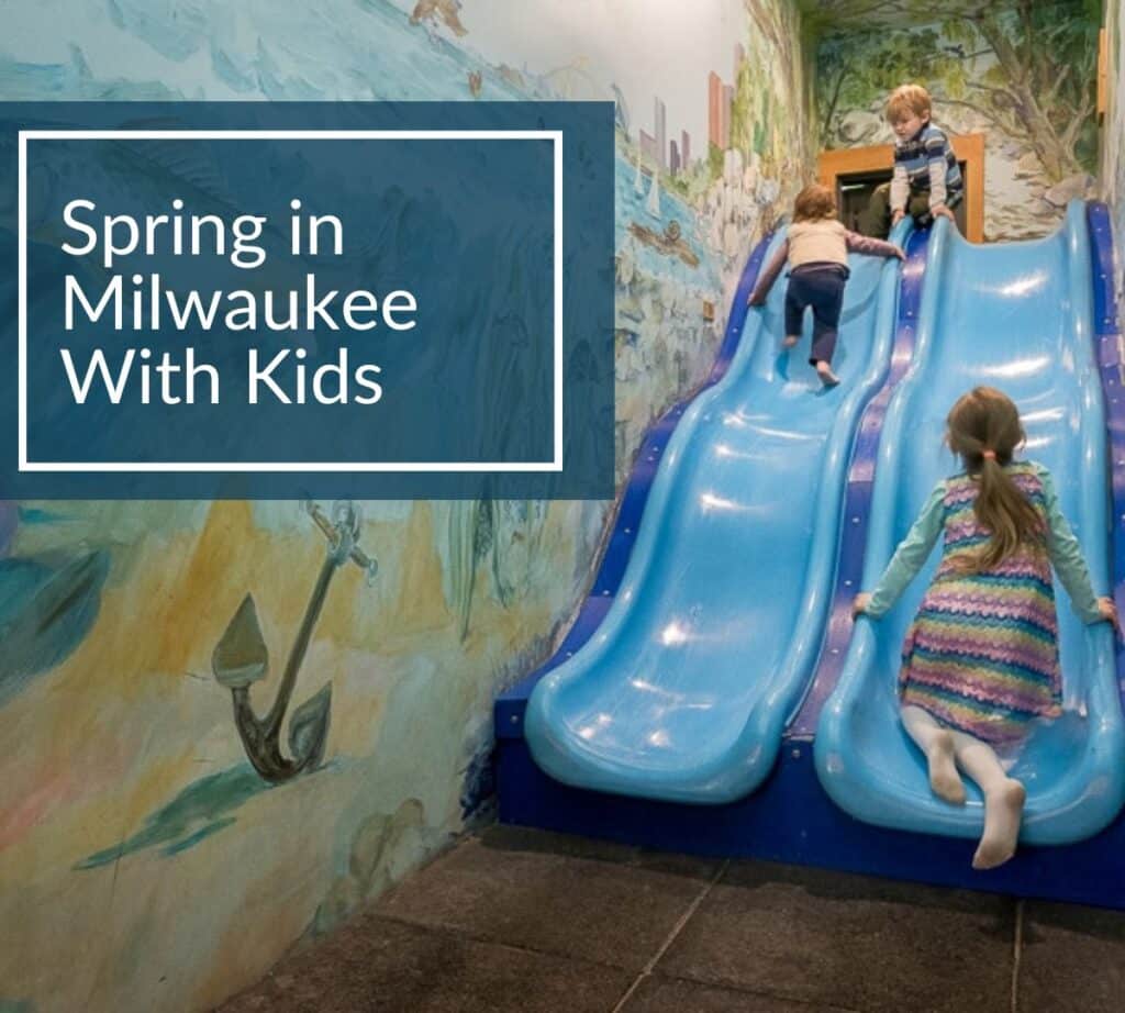 Children playing on bright blue slides at a Milwaukee indoor play area at the Urban Ecology Center, with a text overlay that reads ‘Spring in Milwaukee With Kids.’