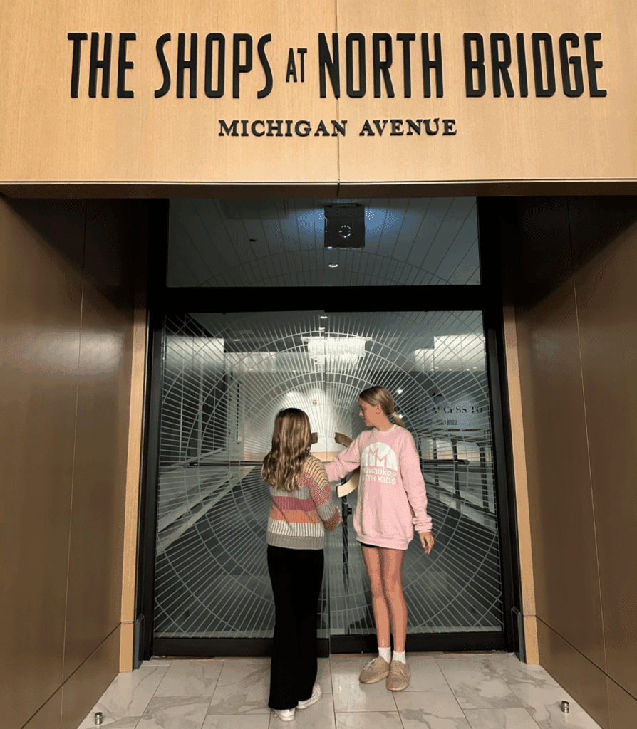 Two girls standing at The Shops at North Bridge entrance on Michigan Avenue, accessible directly from The Gwen Chicago.
