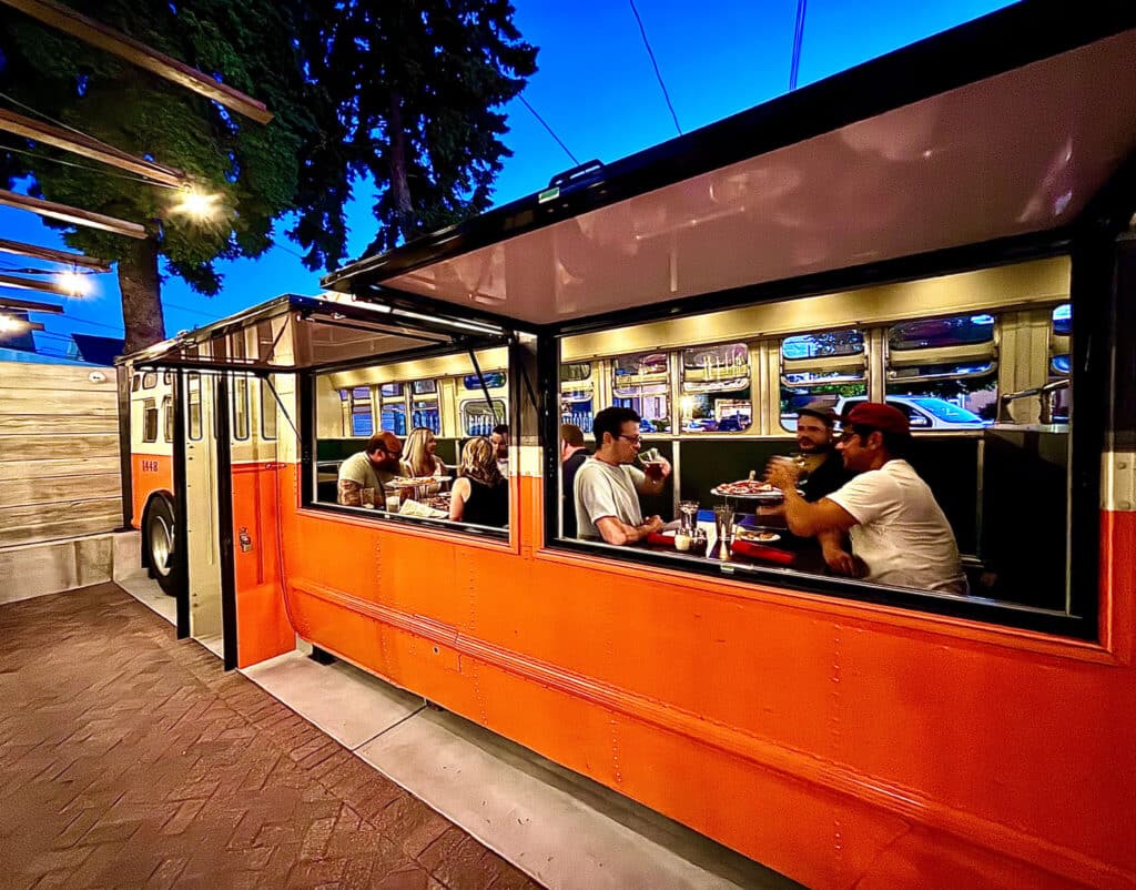 People eat pizza in an old refurbished bus that is bright orange at Transfer Pizzeria in Milwaukee Wisconsin.