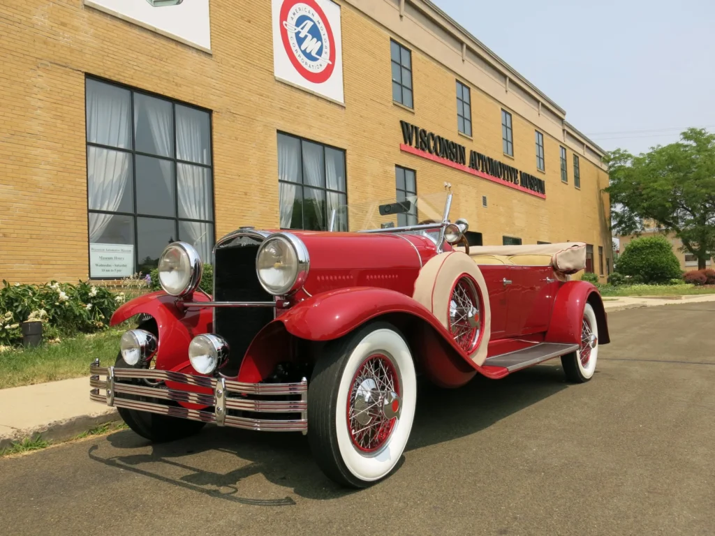 A vintage red and white convertible parked in front of the Wisconsin Automotive Museum.