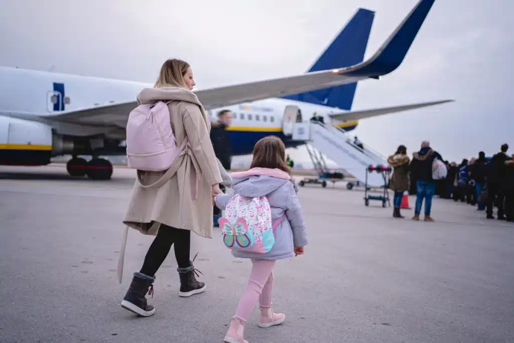 Parent and toddler walking down an airplane aisle together.