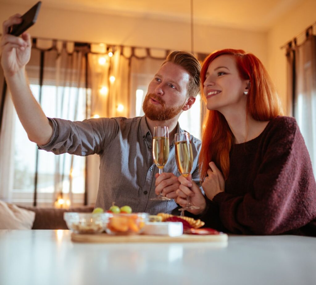 Couple enjoying an at-home date night with wine and snacks while taking a selfie.