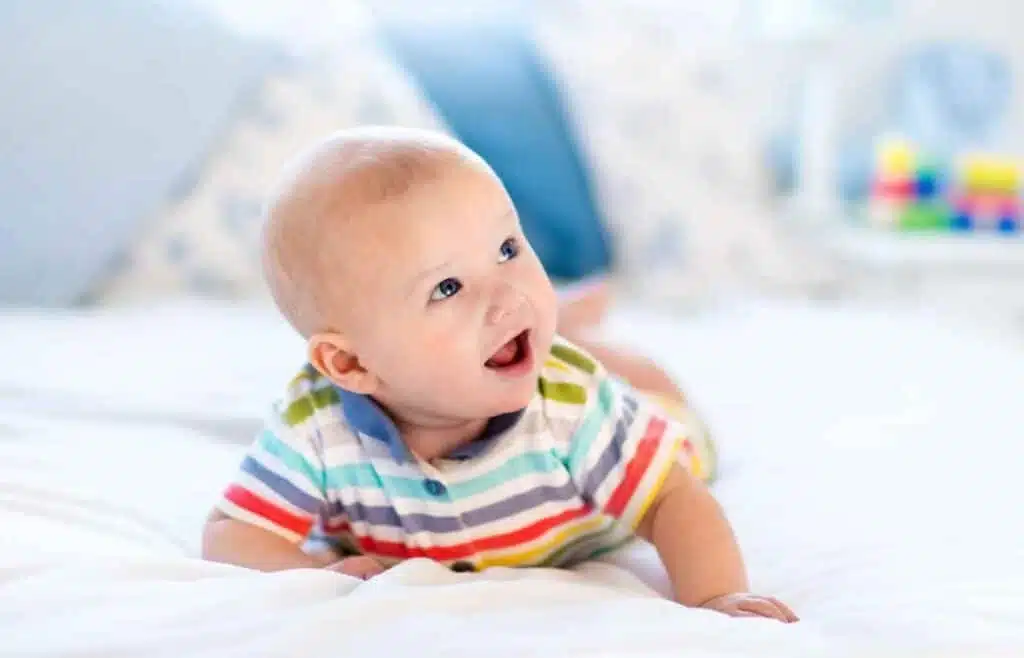 A baby boy in colorful outfit crawing on a white blanket