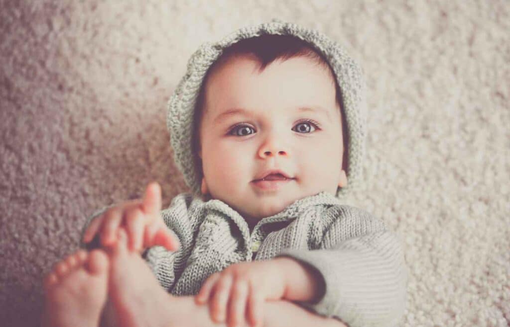A baby boy with blue eyes wearing a light sage knitted clothes and cap 