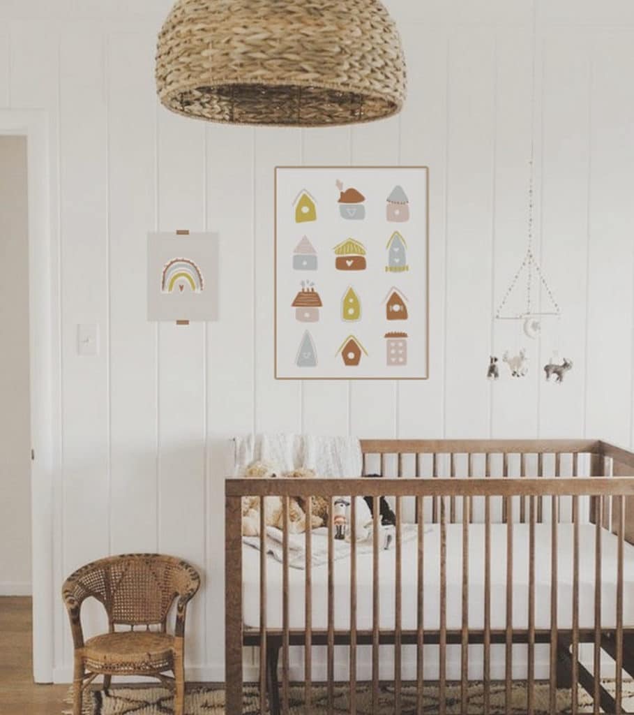 Boho chic baby girl nursery with earthy tones, natural wood crib, wicker basket, and wall art featuring pastel birdhouses.