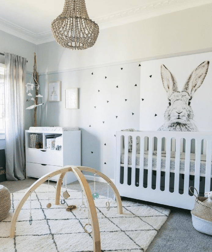 Baby girl nursery with large bunny wall paper, minimalist white crib, play rug with diamond design and sheer curtains inspired by the cozy bunny design.