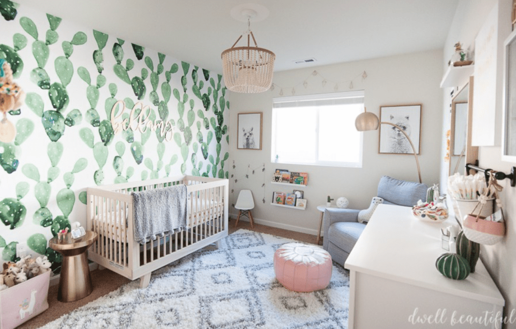 Baby girl nursery featuring white crib, and woven and gold accents and a cactus mural accent wall.