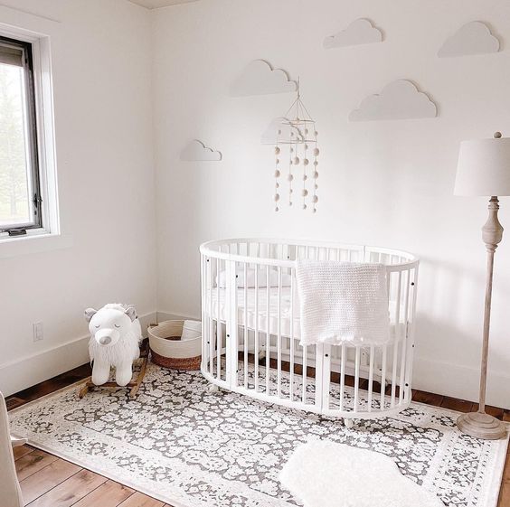 Baby girl nursery with minimalist crib, white floor lamp and white sky wall mural inspired by clouds