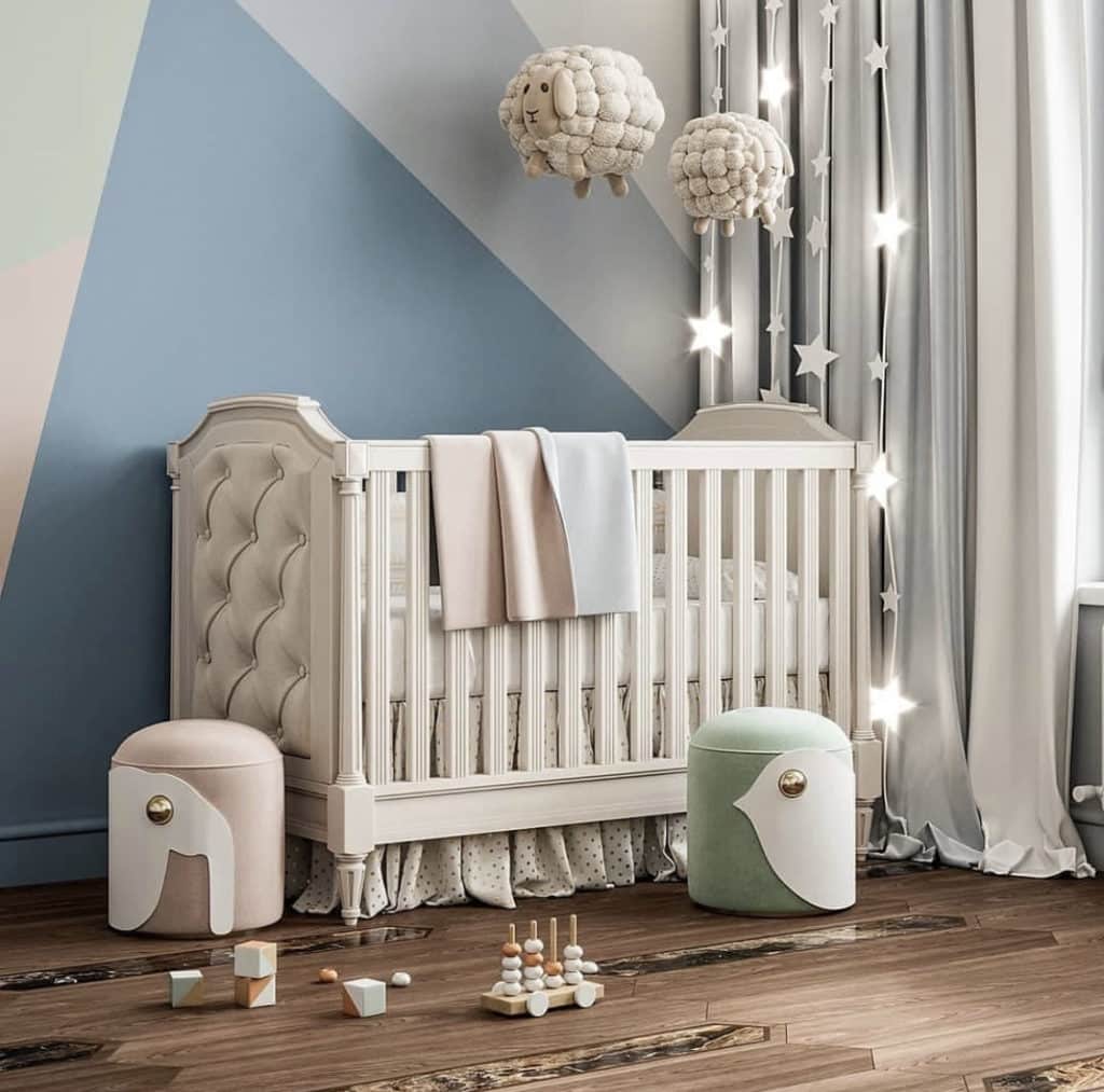 Baby girl nursery with muted blue and grey walls, white crib, wooden floors and ivory curtains with stuffed sheep crib mobile to represent the counting sheep theme.