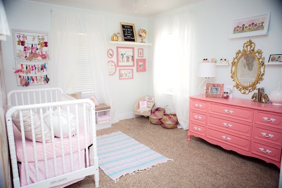 Baby girl nursery with pink chest of drawers, iron crib, mirror with gold accent and pink picture frames on the wall inspired by family's heritage.