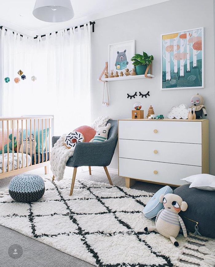 Baby girl nursery with sheer curtains, whimsical wall decor, plush carpet and knitted poufs inspired by Nordic whimsy design.
