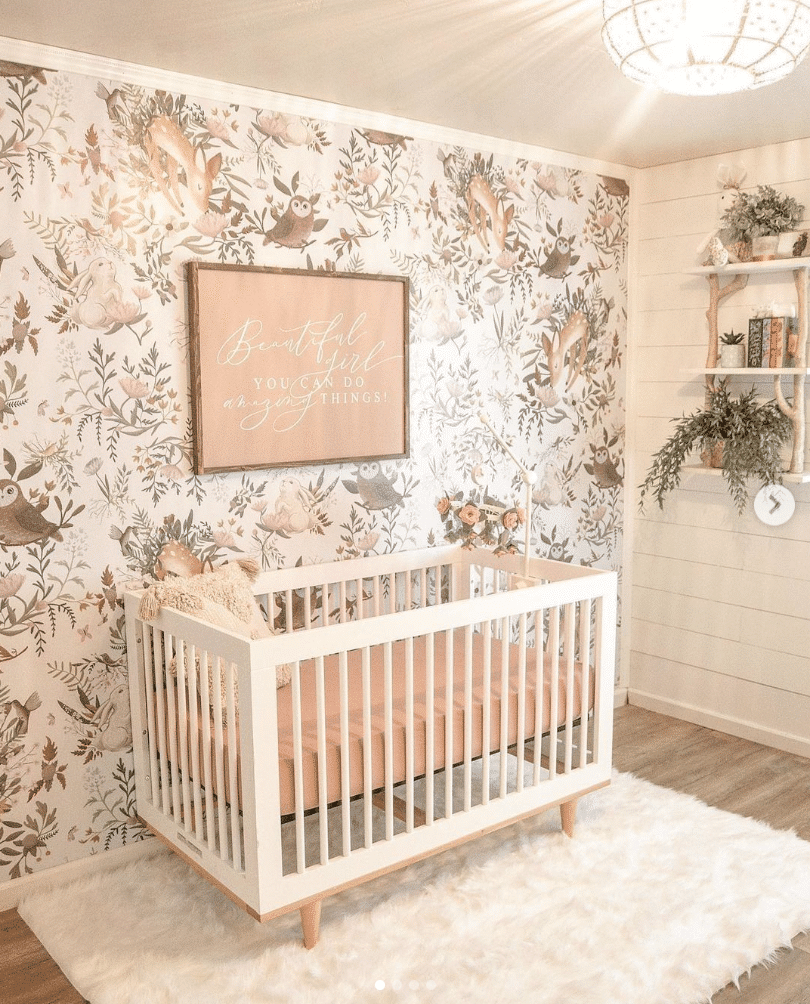 Baby girl nursery with forest inspired wall paper, crib with beige mattress and shelving with potted plants inspired by owls.
