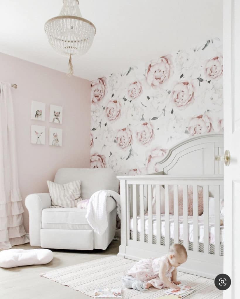 Baby girl nursery with white couch, crystal chandelier and crib set against pink floral mural wall accent inspired by peonies.