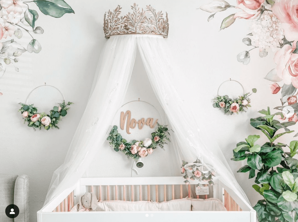Baby girl nursery with pink and green botanical decor and white crib with a canopy crown, inspired by a fairytale princess theme.