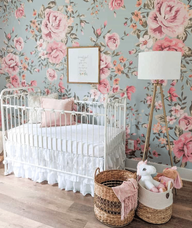 Baby girl nursery with tall stand lamp, retro style white crib, wooden floors , raffia floor baskets and antqie style floral wallpaper representing vintage roses.