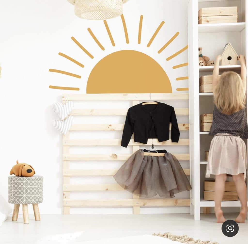 Baby girl nursery with a minimalist sunburst decal and wooden pallet rack used, showing airy and cheerful vibe of the sunshine inspired room