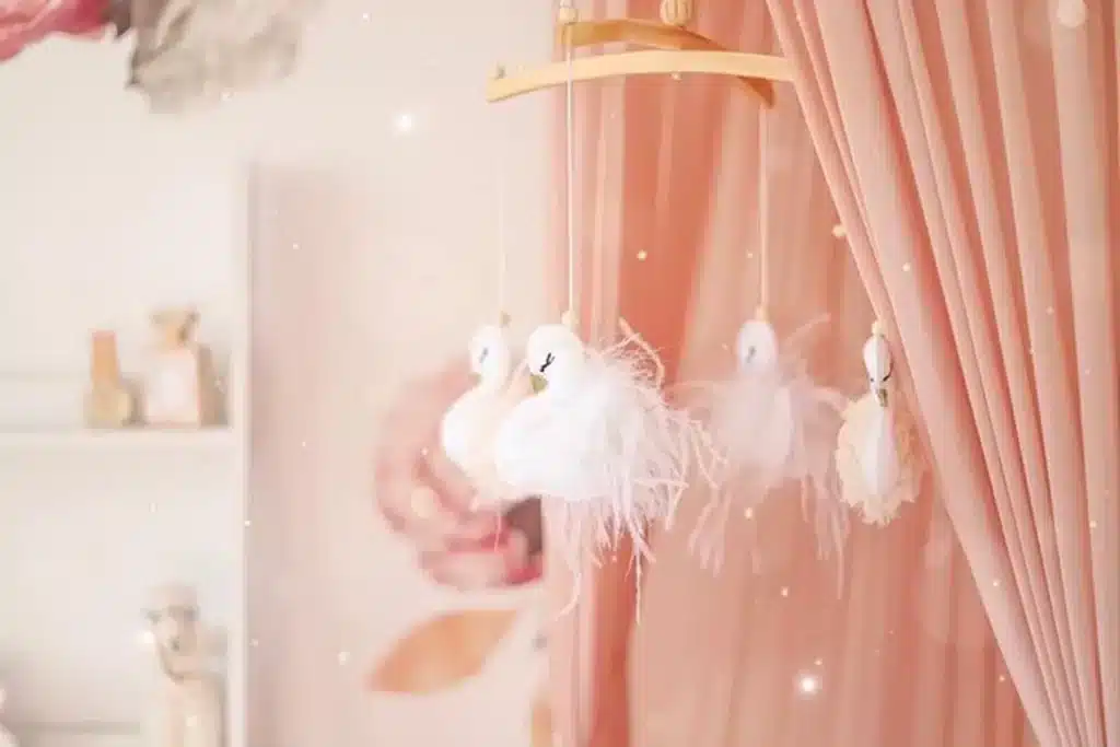 Baby girl nursery with soft peach canopy, white open cabinets and white  crib mobile inspired by swans.