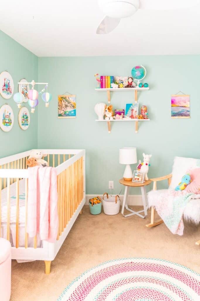Baby girl nursery with mint green walls, brown carpets, shelving with globe, bright books and hot balloon mobile inspired by traveling.