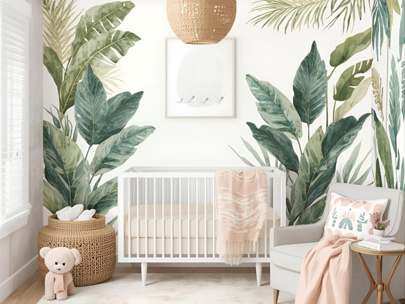 Baby girl nursery with large leaf wall decals, wicker basket, muted grey couch and round side table with gold legs inspired by the tropical design.