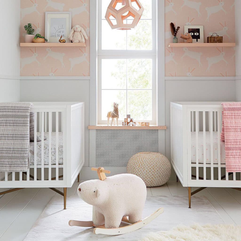 Baby girl nursery with soft pink bunny wallpaper, white cribs, and natural wood accents showing the wallpaper trend for 2026.