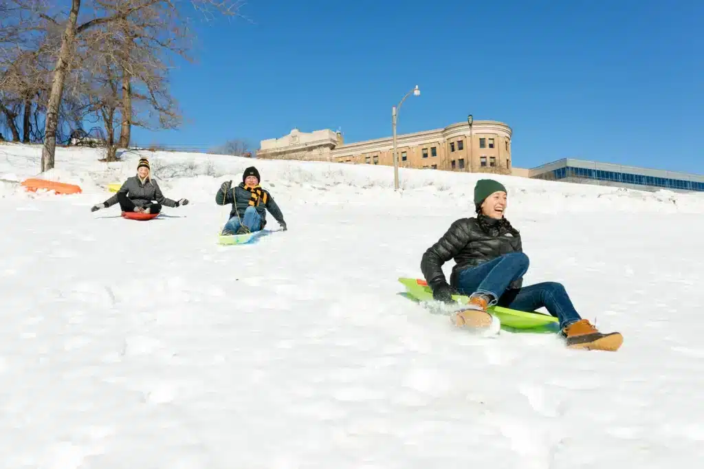 Teens sledding downhill at Back Bay Park on a sunny winter day