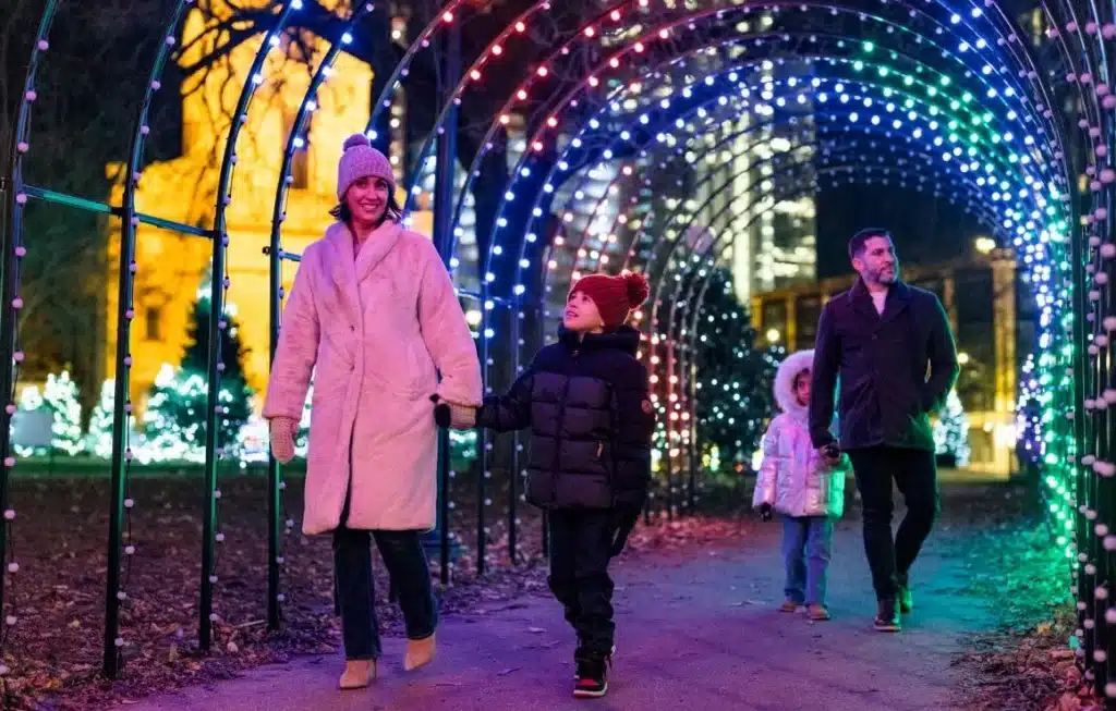 Mother, father, son and daughter walking through a passageway decorated with Christmas lights in different colors