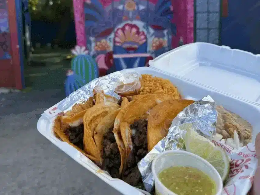 Birria tacos with rice, beans, lime, and salsa in a takeout container.