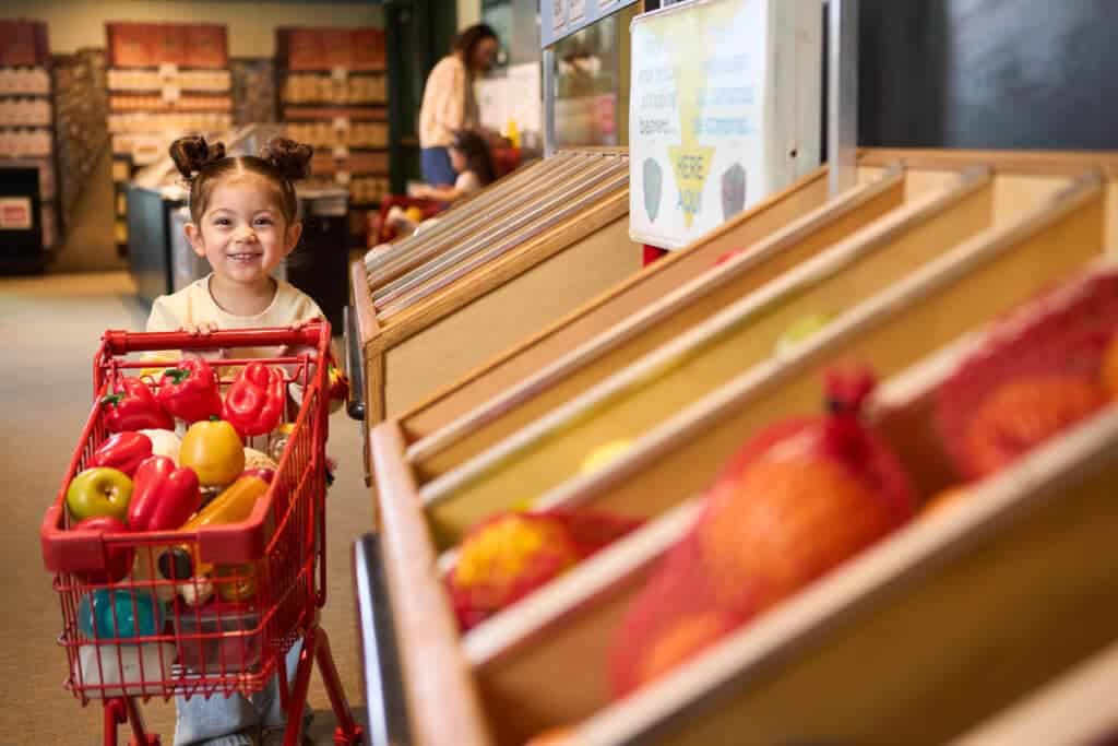 Child grocery shopping in the Home Town exhibit at Betty Brinn Children’s Museum