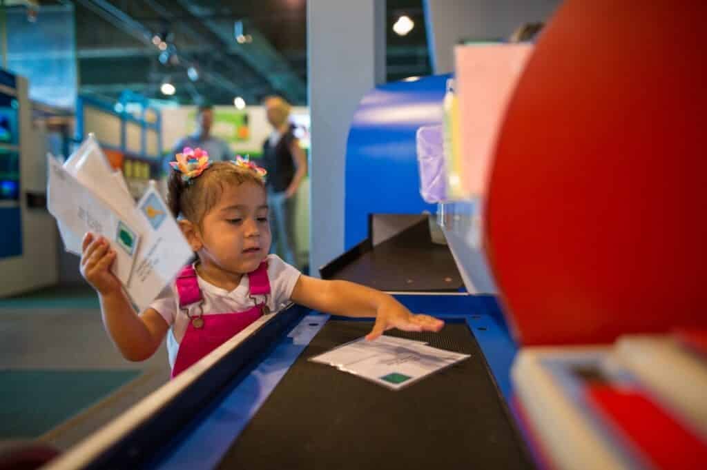 A little girl in fuschia jumpsuit playing with cardboards, an activity kids with family memberships can enjoy at Betty Brinn Children's Museum.